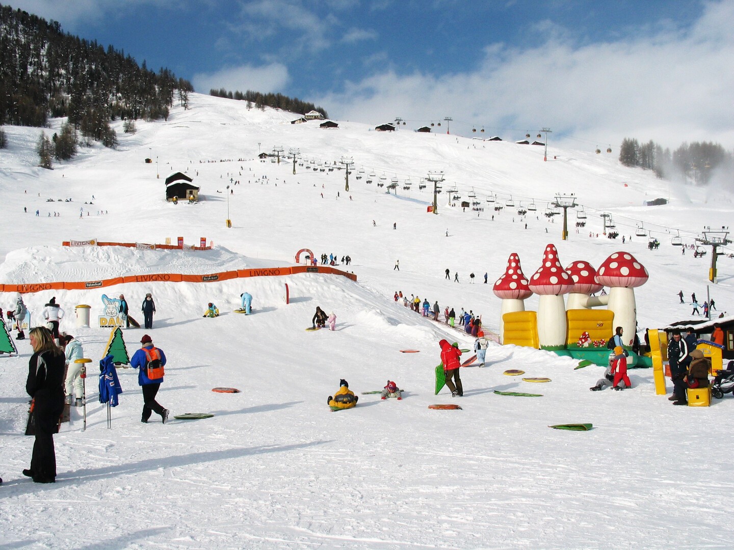 Familles et enfants profitant d’une journée ensoleillée à la neige, avec un espace de glisse ludique, des structures gonflables et des pistes idéales pour les débutants.