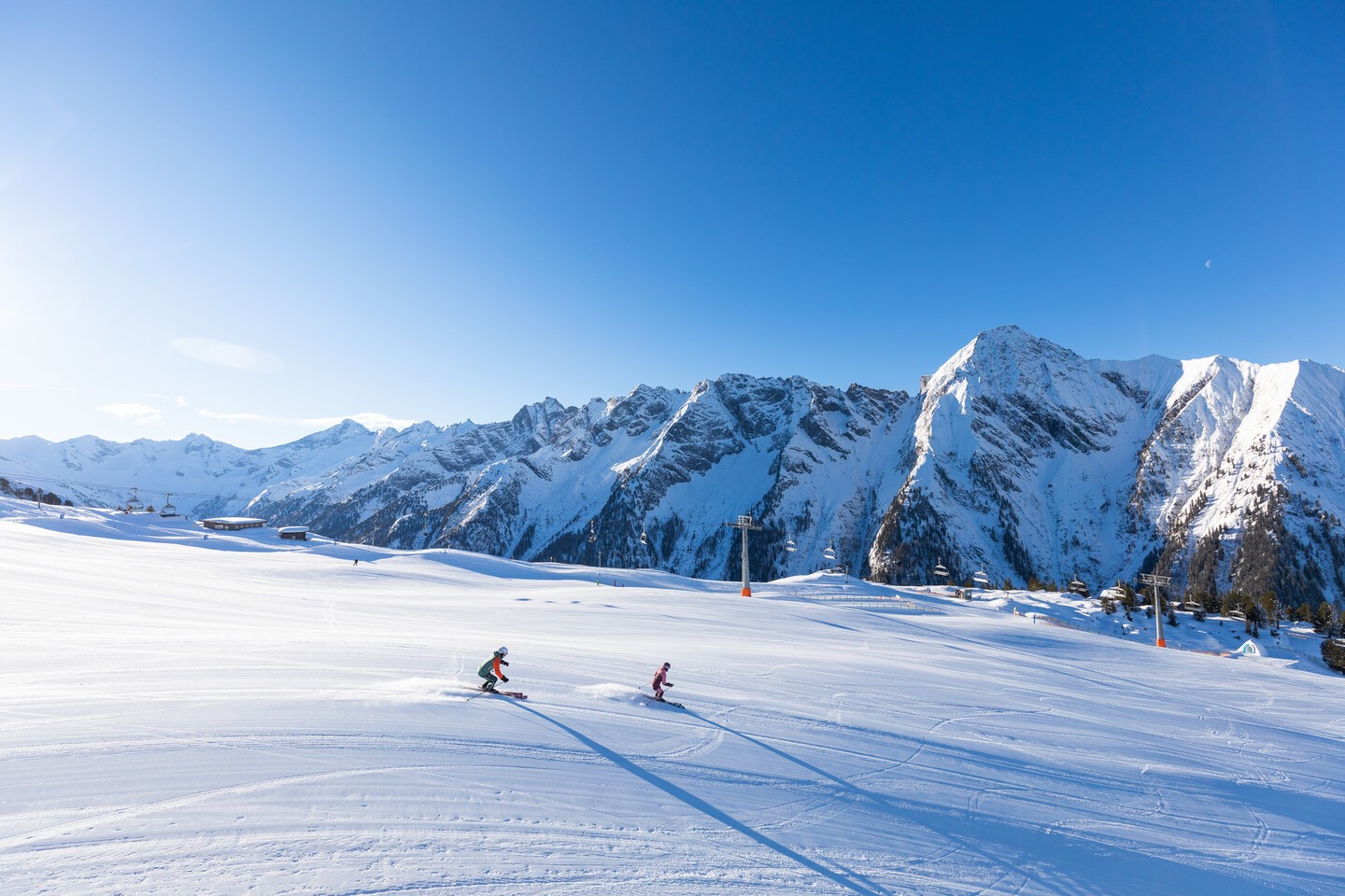 Deux skieurs dévalant une piste immaculée dans un paysage de montagne enneigé, sous un ciel bleu éclatant, symbole d’un séjour de ski réussi.